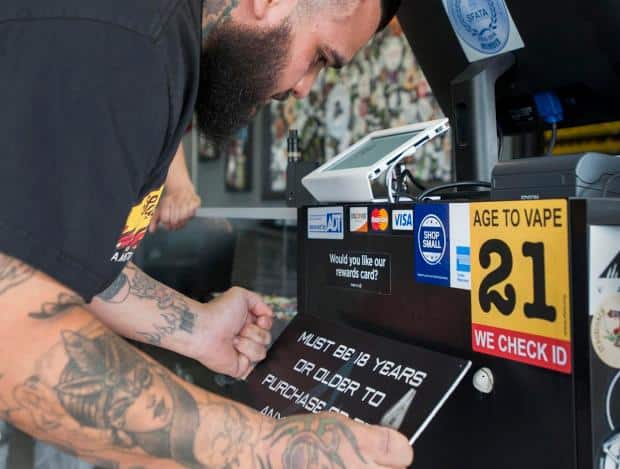 Vape Shop Clerk at Point-of-Sale with We Check ID Sticker